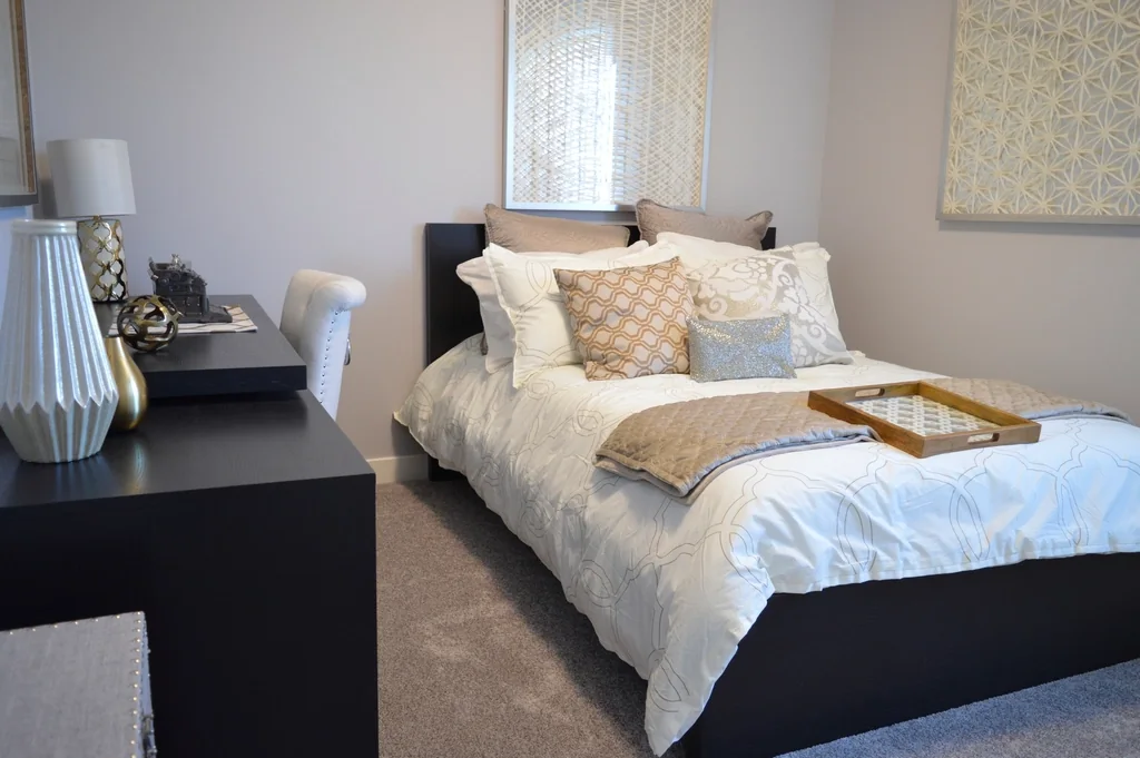A bright bedroom with a made bed, a desk and soft daylight